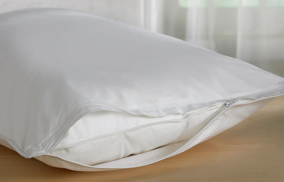 A zippered pillow protector being placed over a clean new pillow