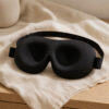 Black 3D contoured sleep mask on warm neutral linen